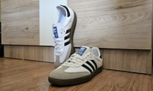 Adidas Sneaker mit schwarzen Streifen auf Holzfu&szlig;boden vor modernem M&ouml;bel