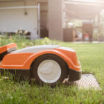 Ein orangefarbener KI-gestützter Mähroboter auf einem Rasen