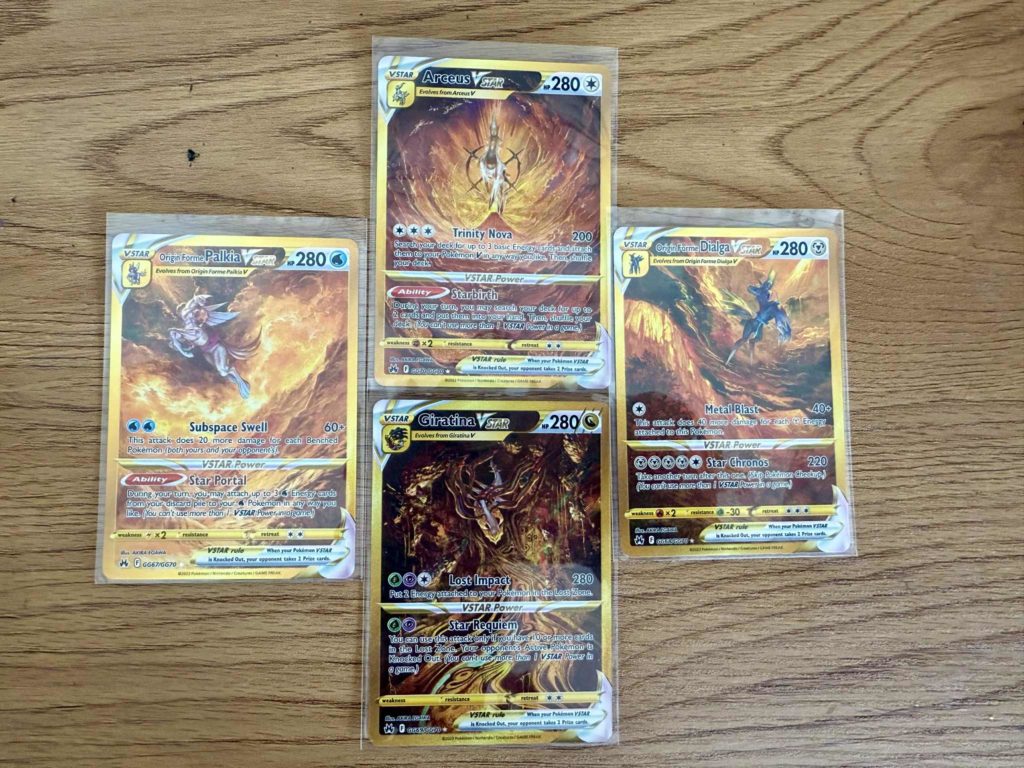 Vier Pokémon-Karten der legendären Pokémon Arceus, Dialga, Palkia und Giratina in Hüllen auf Holzoberfläche.