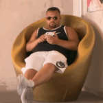 Menowin Fröhlich sitzt entspannt in einem gelben Designersessel, trägt Sportkleidung und Sonnenbrille.